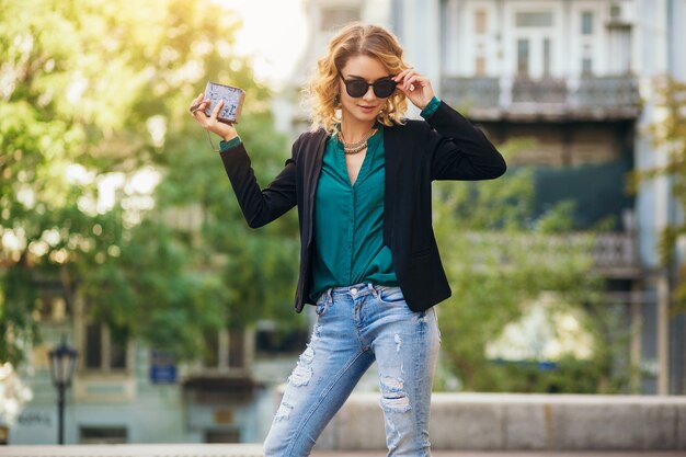 Attractive elegant woman walking in city street with purse, wearing black jacket, confident and sexy,