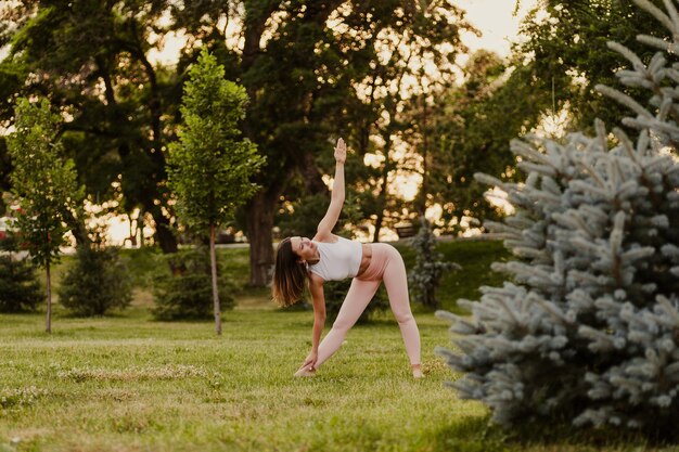 Attractive elegant woman do yoga and stands in trikonasana pose while maintaining balance on green g...