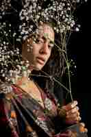 Бесплатное фото Привлекательная этническая очаровательная женщина с цветочными ветками в темноте