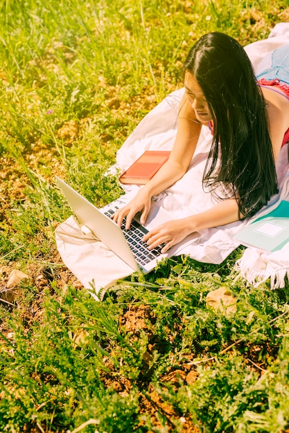Foto gratuita femmina etnica attraente che utilizza computer portatile nel prato