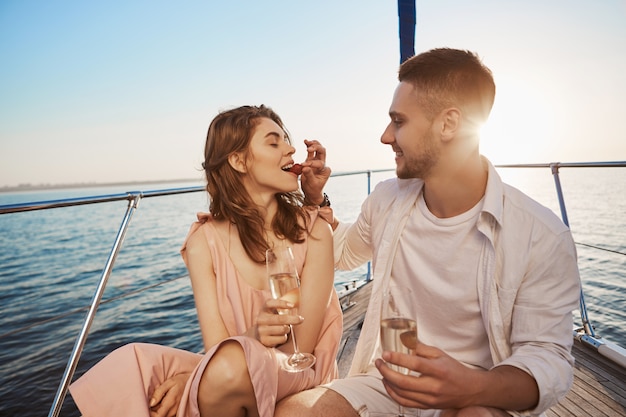 Foto gratuita attraente coppia europea in vacanza estiva, godendo la navigazione a bordo di yacht, bevendo chapmaign. il ragazzo le ha promesso di trascorrere le vacanze insieme, quindi ha acquistato un tour in barca.