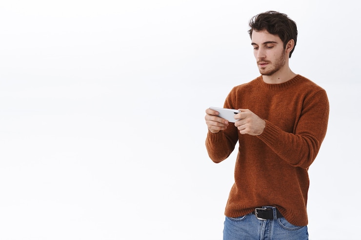 Free Photo attractive european guy using mobile phone, hold smartphone horizontally and look display focused on passing level