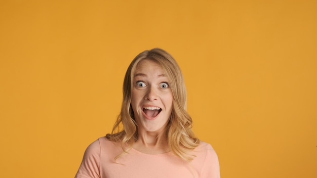 Attractive excited blond girl keep mouth open surprisingly looking in camera over colorful background Copy space for text or advertising content