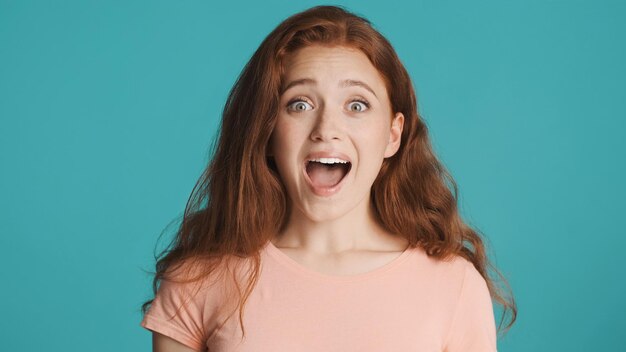 Attractive excited redhead girl surprisingly looking in camera over colorful background Rejoicing expression