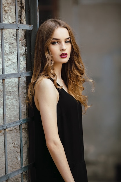 Бесплатное фото Привлекательная модная женщина в черном платье позирует возле белой стены