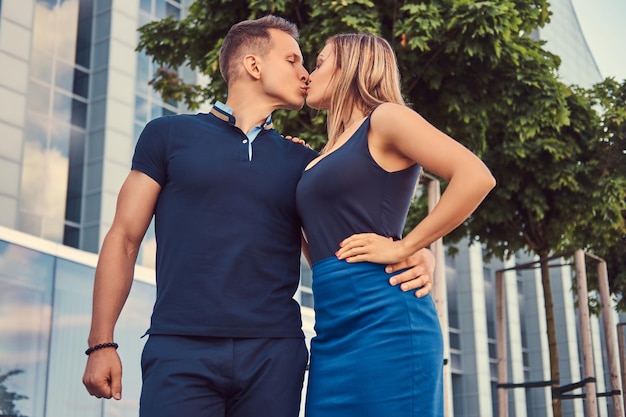 Привлекательная модная пара, сексуальная блондинка и красивый мужчина, целующиеся в современном городе на фоне небоскреба.