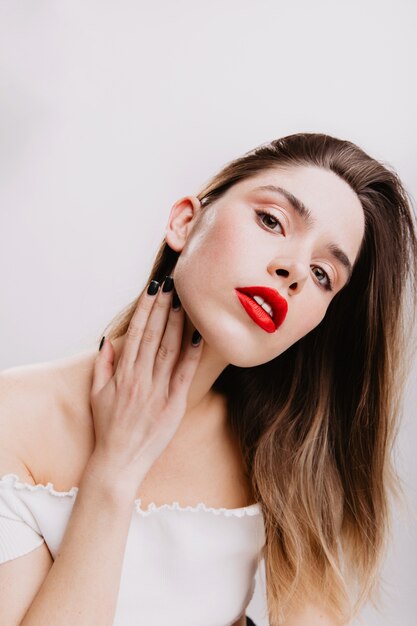 Attractive fashionable girl with red lipstick proudly on white wall.