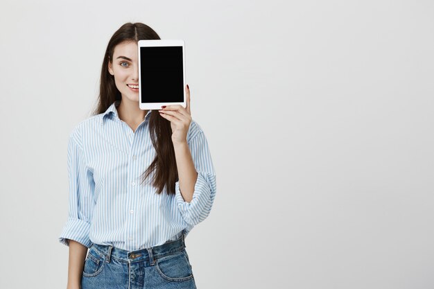 Attractive female cover half of face with digital tablet, showing display