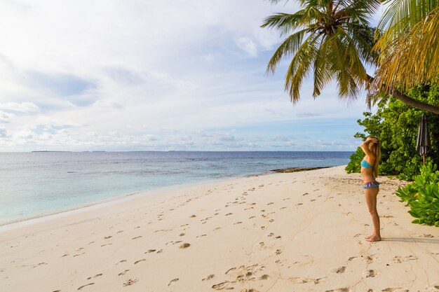 Attractive female in a cute swimsuit standing on the beach by the ocean