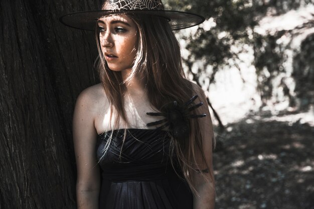 Attractive female in hat and decorative spider on shoulder looking away