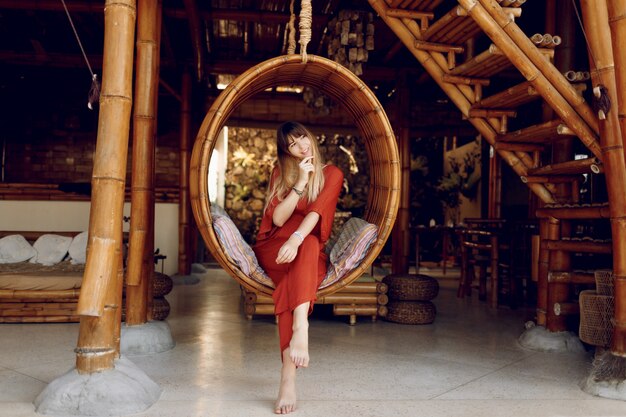 Attractive female siting in hanging bamboo stair on open-air veranda of wooden bungalow