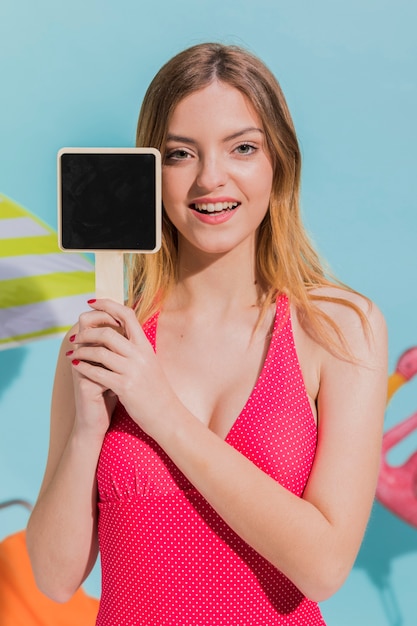 Free photo attractive female in swimsuit holding blank sign