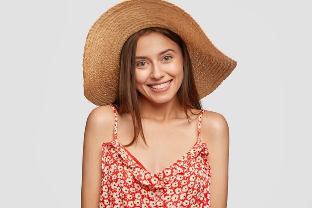 Attractive female traveler with friendly pleasant smile, wears stylish hat, dressed in fashionable dress