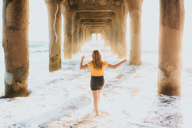 An attractive female in a yellow t-shirt and short shorts standing under a large stone pier