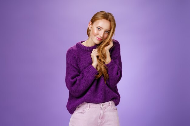 Привлекательная женственная и застенчивая рыжая девушка флиртует мило и нежно в камеру, играя с гребнем волос, кокетливо и глупо позирует на фиолетовом фоне.