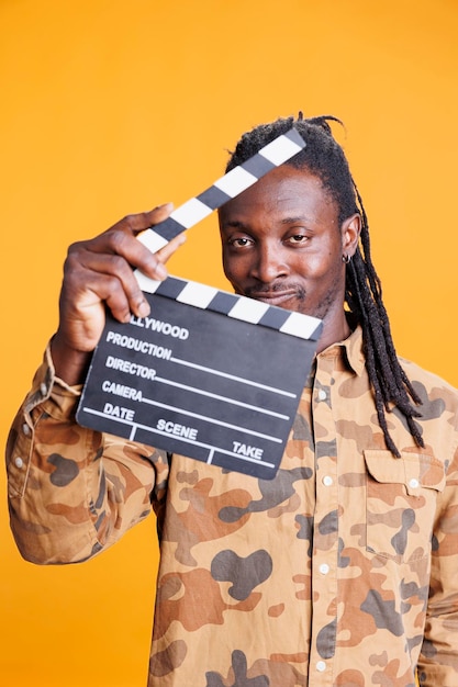 Free photo attractive film director holding clipper board to cut scenes in movie making industry. african american man presenting chalkboard to camera and smiling while having filmmaker object. cinema concept