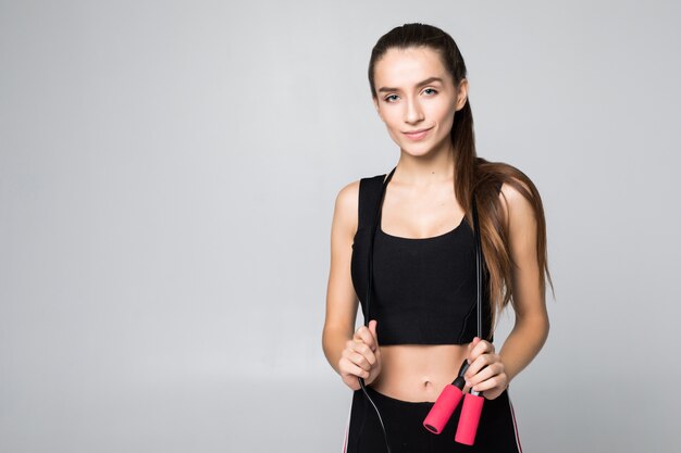 Attractive fitness woman in the air jumping rope isolated on white wall