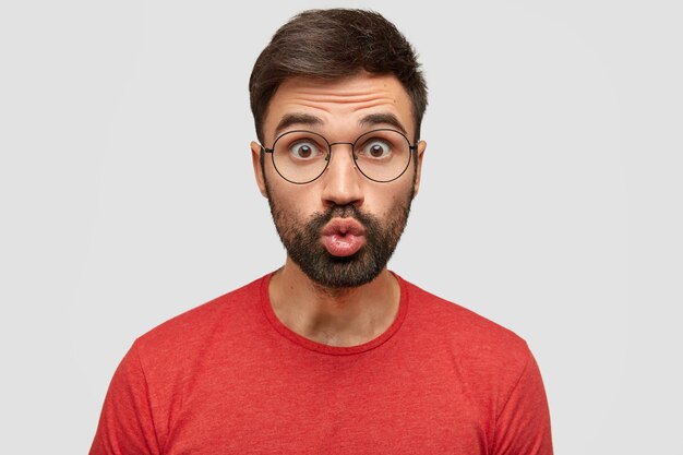 Attractive funny man with surprised expression keeps lips rounded, sends kiss,