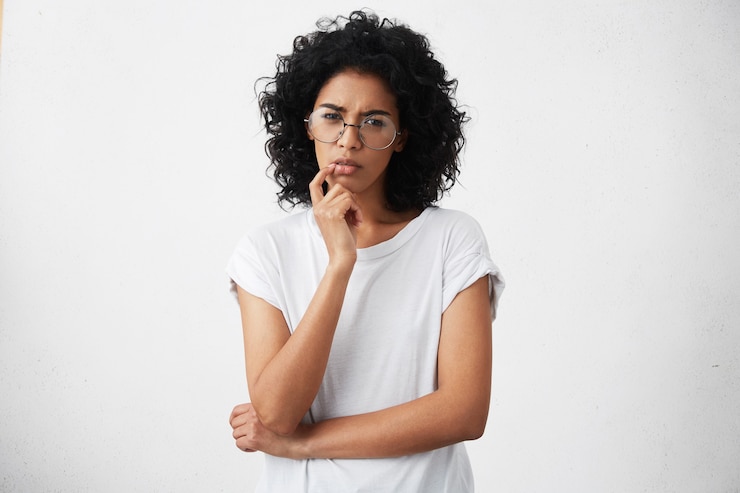 Free Photo attractive girl in casual t-shirt and round glasses squeezing eyes and keeping hand on chin
