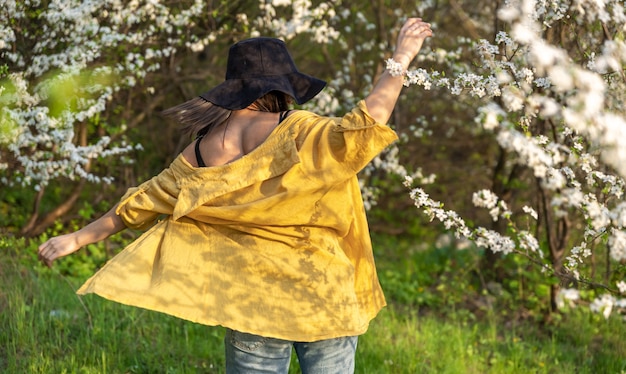 Una ragazza attraente con un cappello tra alberi in fiore gode dell'odore dei fiori primaverili