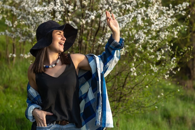 Attractive girl in a hat among the flowering trees in the spring, in a casual style