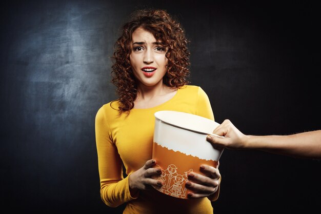 Attractive girl looks sad striving for popcorn bucket with friend