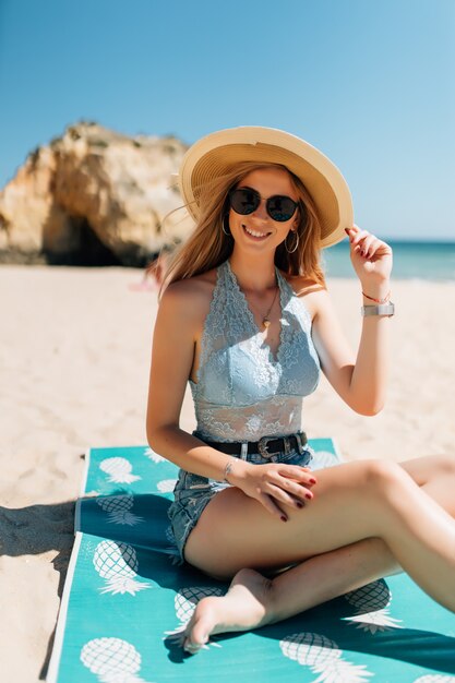 Attractive girl in sunglasses and hat lies on warm sand