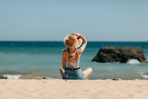 Free photo attractive girl in sunglasses and hat lies on warm sand