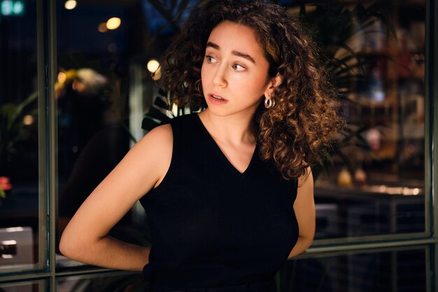 Attractive girl thoughtfully looking away waiting washing in modern self-service laundry at night