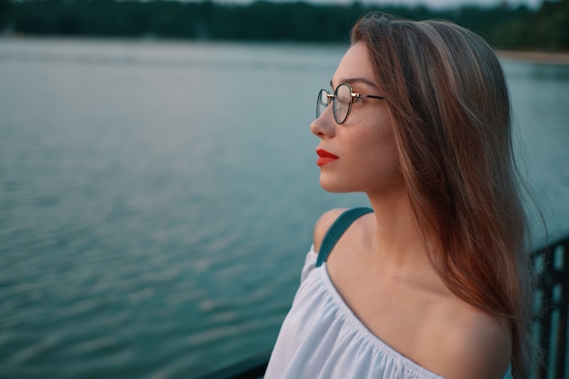 公園の湖の景色に眼鏡をかけている魅力的な女の子