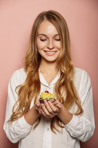 白いシャツで魅力的な女の子がカップケーキを保持しています。