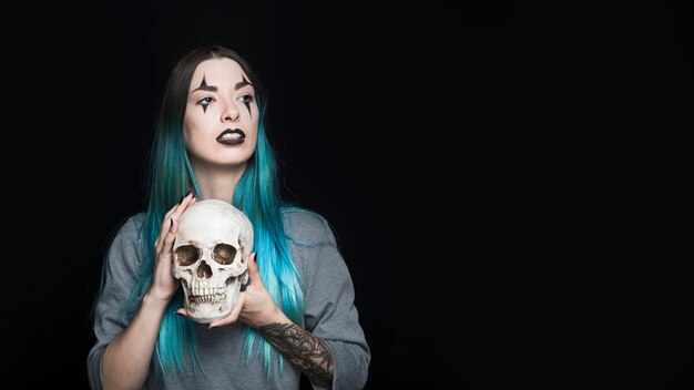 Attractive girl with harlequin makeup holding skull