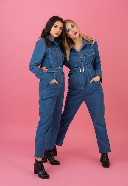 Attractive girls posing on pink background in denim overall fashion trend