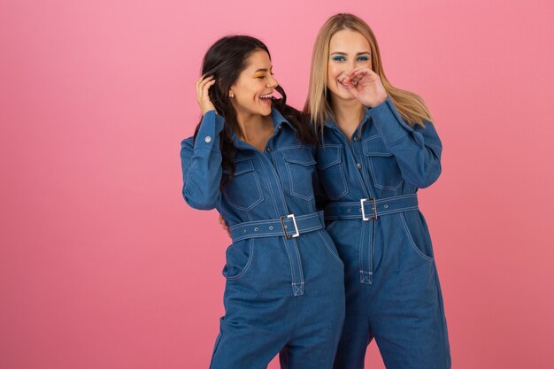 Attractive girls posing on pink background in denim overall fashion trend