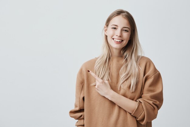 attractive good-looking smiling young woman in casual clothes pointing with index finger up having pleased look, with cheerful and happy expression of face.