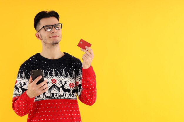 Привлекательный парень с кредитной картой и телефоном на желтом фоне