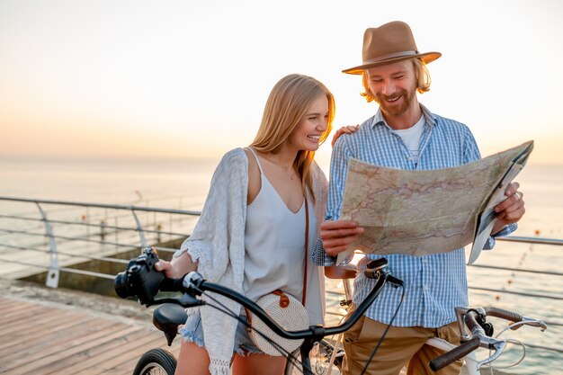 Attractive happy couple of friends traveling in summer on bicycles, man and woman with blond hair boho hipster style fashion having fun together