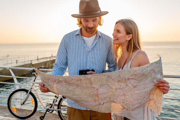 Attractive happy couple traveling in summer on bicycles, man and woman with blond hair boho hipster style fashion having fun together, looking in map sightseeing