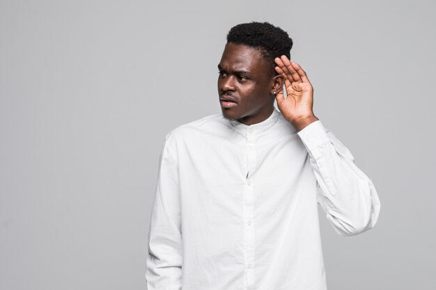 Attractive happy dark-eyed afro-american man smiling and having his hand hear his ear and showing that he cant hear isolated gray background