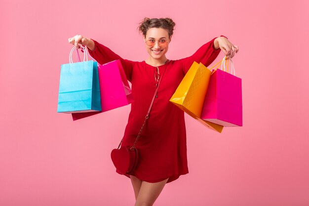 Attractive happy funny emotion stylish woman shopaholic in red trendy dress holding colorful shopping bags on pink wall isolated, sale excited, spring summer fashion trend