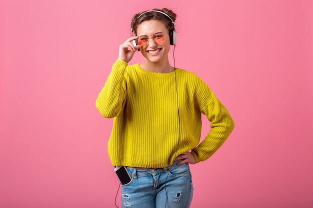 노란색 스웨터와 선글라스를 착용, 재미, 분홍색 벽에 고립 힙 스터 화려한 스타일의 옷을 입고 헤드폰에서 음악을 듣고 매력적인 행복 재미있는 여자
