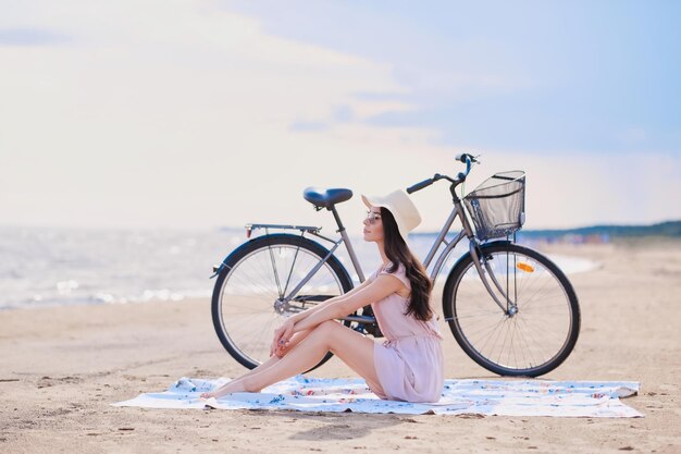 Привлекательная счастливая девушка отдыхает на пляже со своим велосипедом после долгой прогулки по берегу моря.