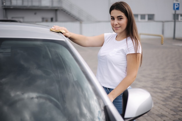 魅力的な幸せな楽しい女性ドライバーは セルフサービスの洗車でぼろきれを使用して彼女の車のフロントガラスを拭きます プレミアム写真