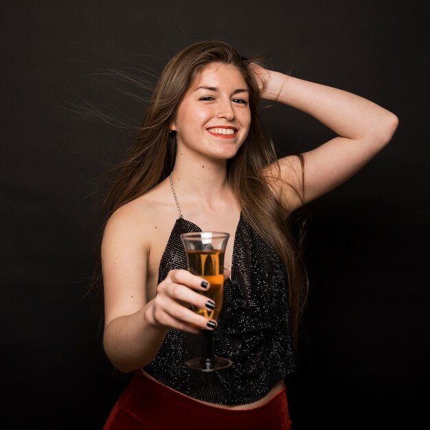 Attractive happy lady in evening cloth with glass of drink and hand on head 