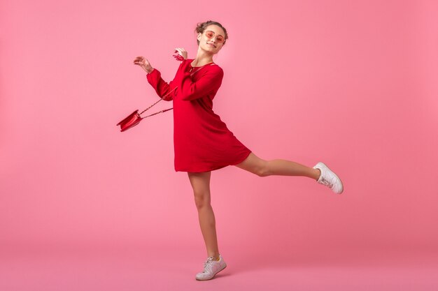 Attractive happy smiling stylish woman in red trendy dress jumping running on pink wall isolated, spring summer fashion trend, romantic mood flirty girl