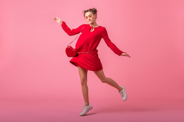 Attractive happy smiling stylish woman in red trendy dress jumping running on pink wall isolated, spring summer fashion trend, Saint valenite's day, romantic mood flirty girl