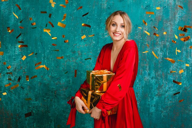 Attractive happy smiling woman in stylish red dress celebrating christmas and new year with gifts