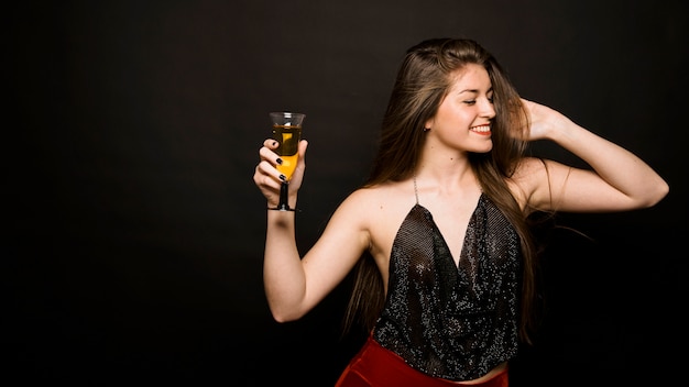 Attraente donna felice in panno di sera con un bicchiere di bevanda e la mano sulla testa