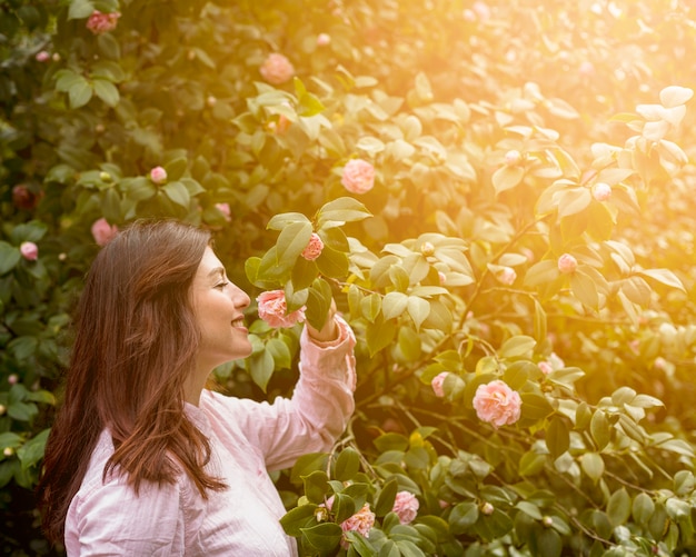 Привлекательная счастливая женщина, держащая розовое цветущее растение на зеленой ветке
