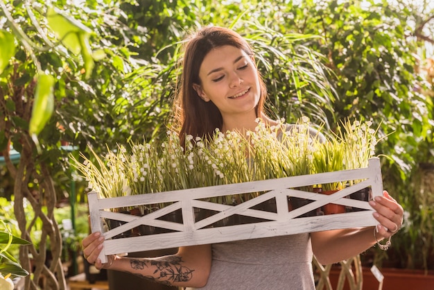 Attractive happy woman holding wooden shelf with plants